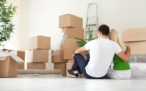 Couple sitting in room full of moving boxes — Stock Photo, Image