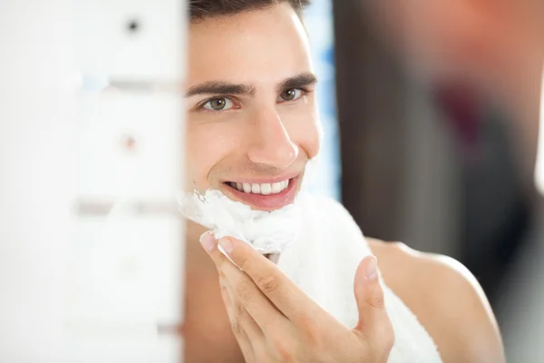 Jovem aplicando creme de barbear em seu rosto — Fotografia de Stock