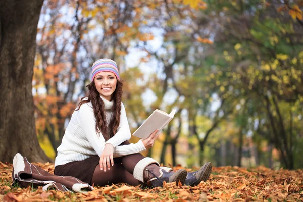 Mujer sonriente con libro en el parque de otoño — Foto de Stock