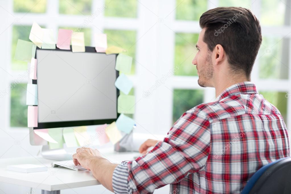 Man looking at a monitor with sticky note on it