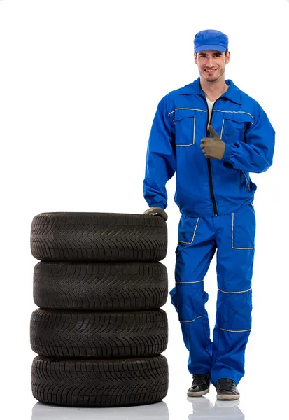 Jovem mecânico de carro com pneus de carro de pilha — Fotografia de Stock