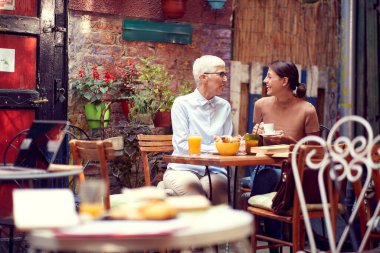 Kafkasyalı anne ve kız birlikte kahvaltı yapıyorlar, birbirlerine bakıyorlar, konuşuyorlar, gülüyorlar, gülüyorlar.