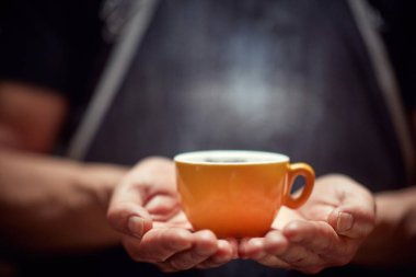 Barista elinde sarı bir fincan koyu kahve tutuyor. 