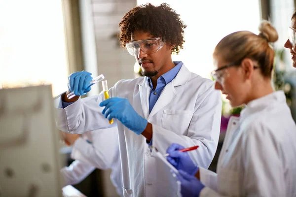 Young students mixing chemicals in a test tube and taking notes about a chemical reaction in a sterile environment of the laboratory. Science, chemicals, lab, people