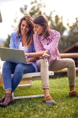 Güzel, güneşli bir günde bahçede birlikte vakit geçirirken dizüstü bilgisayarın içeriğini izleyen bayan arkadaşlar. Arkadaşlık, birlikte, eğlence.