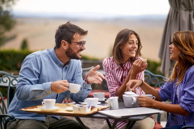 Güneşli bir günde bir grup neşeli arkadaş barın bahçesinde kahve içiyor. Arkadaşlık, birlikte, eğlence.