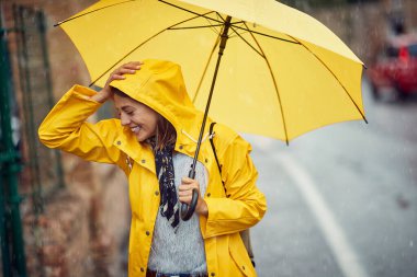 Neşeli beyaz kadın şehirde yağmurlu bir günün tadını çıkarıyor.