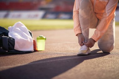 Genç bir kız stadyumda güzel bir gün için spor antrenmanına hazırlanırken ayakkabılarını sıkıyor. Spor, atletizm, sporcular