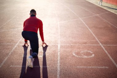 Stadyumdaki güzel bir günde antrenman sırasında yarış pistinde düşük bir başlangıç yapan genç bir atlet. Spor, atletizm, sporcular