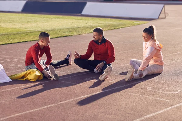 caucasian personal trainer talking, explaining with hand gesture to young adult couple, preparing for training, stretching