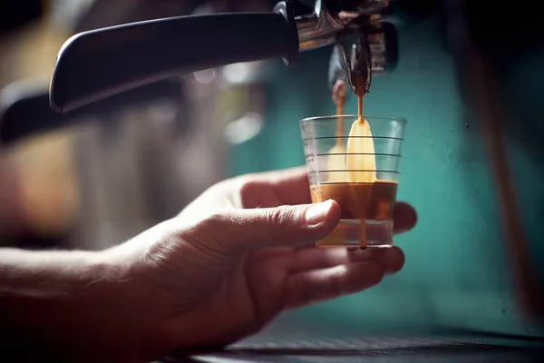 バーマンは小さなガラスを保持し エスプレッソ機器で芳香族と香りの飲料でそれを充填しています コーヒー — ストック写真