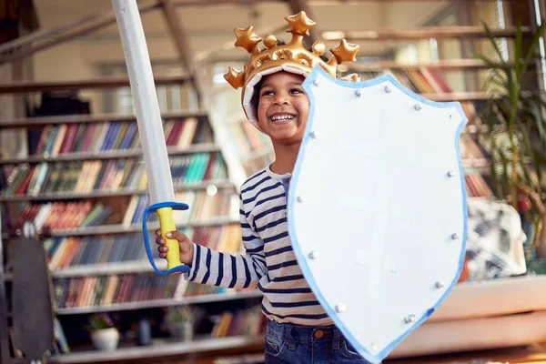 Şövalye gibi giyinmiş neşeli küçük bir çocuk evde rahat bir atmosferde oyun oynarken fotoğraf için poz veriyor. Aile, ev, oyun zamanı