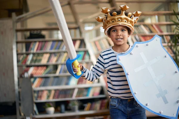 Kılıcı ve kalkanı olan neşeli küçük bir çocuk evde rahat bir atmosferde oynarken fotoğraf için poz veriyor. Aile, ev, oyun zamanı