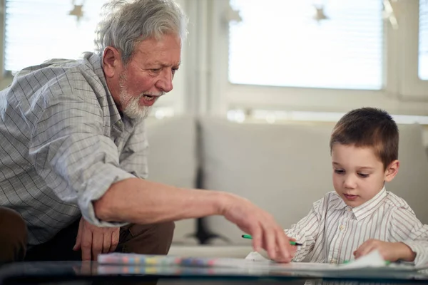 おじいちゃんが孫に絵の描き方を教えていると 家でゆっくりとした時間を過ごすことができます 遊び時間 — ストック写真
