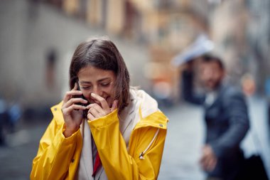 Yağmurlu bir günde, kasvetli bir atmosferde akıllı telefondan konuşan sarı yağmurluk giymiş genç bir kız iyi bir ruh hali içindedir. Yürü, yağmur, şehir
