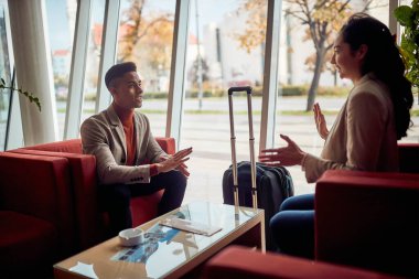 Gülümseyen adam ve kadın bir otelin lobisinde oturuyor.