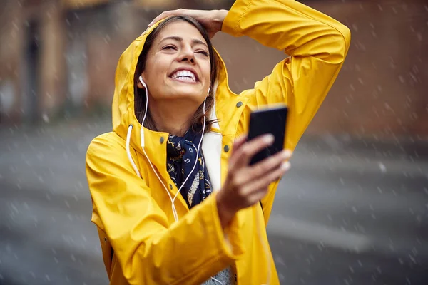 黄色のレインコートを着た若い女の子が音楽を楽しみ 雨の中で平和な雰囲気の中で街を歩く — ストック写真