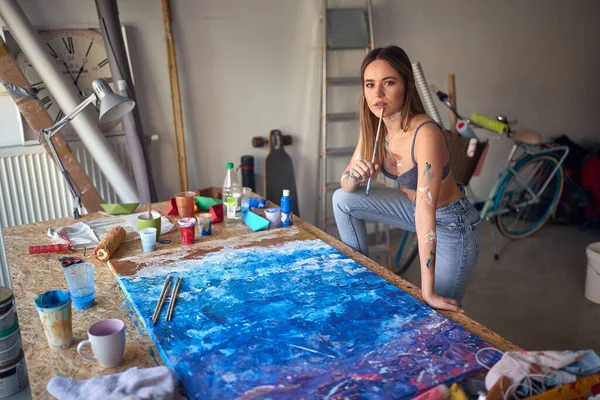 섹시하고 미술가가 테이블 그녀의 스튜디오 분위기에서 그림을 그리는 사려깊게 사진을 — 스톡 사진