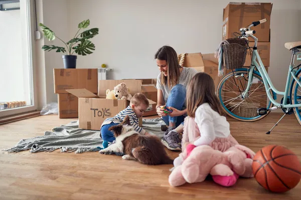 若いお母さんが息子と娘と犬と遊んでる新しいアパートの木製の床に — ストック写真