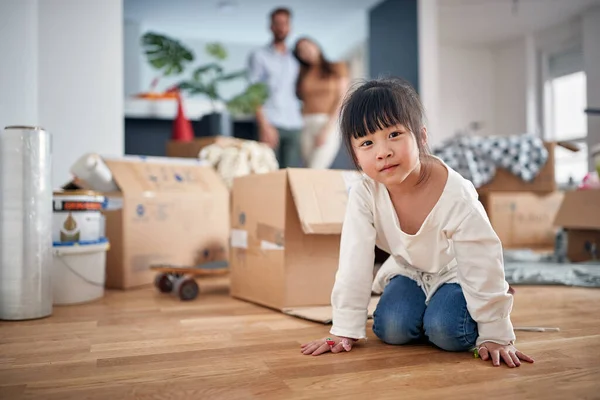 一个小女孩正在一个新家的地板上摆姿势拍照 她和她的父母在愉快的气氛中享受着 — 图库照片