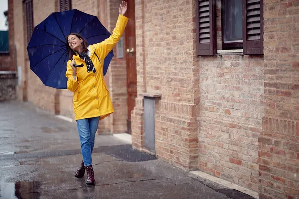 一个身穿黄色雨衣 头戴雨伞的年轻貌美的女人 在下雨天轻松自在地在城里散步时 正在跳舞 — 图库照片