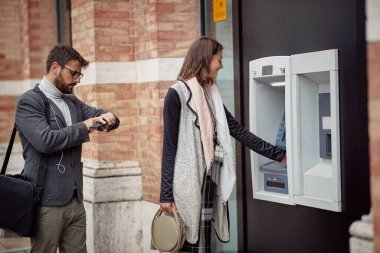 Genç ve zarif bir adam para makinesi için sırada bekliyor ve geç kaldığı için bilek saatini üzgün bir şekilde izliyor. Yürüyüş, ATM, şehir