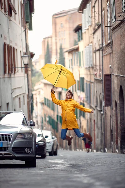 Young Girl Yellow Raincoat Umbrella Jumping Street While Enjoying Walk — Stock Photo, Image