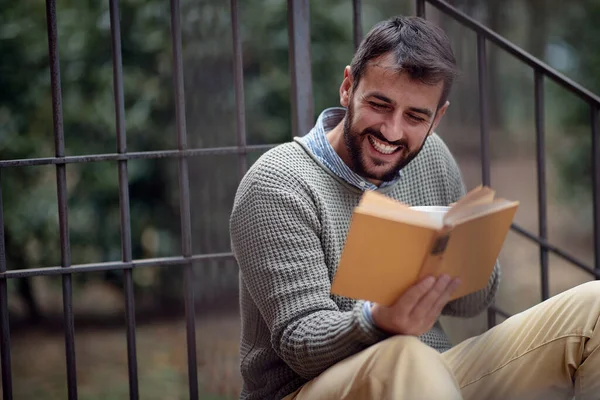 Genç yakışıklı bir adam evin önündeki merdivenlerde rahat bir atmosferde oturup kitap okurken mutlu olur. Şehir, dışarısı, dinlenme