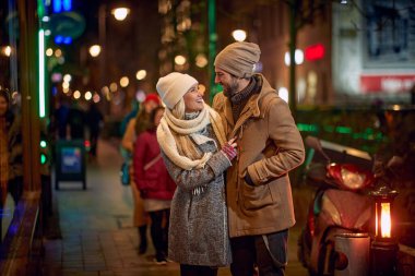 Kış şehrinde yürüyen gülümseyen genç çift