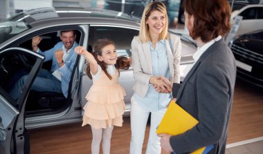 Araba satıcısı yeni araba aldığı için gülümseyen bir kadınla tokalaşıyor.