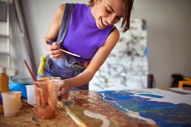 Mutlu genç bir bayan sanatçı stüdyosunda hoş bir atmosferde resim yapıyor. Sanat, resim, stüdyo