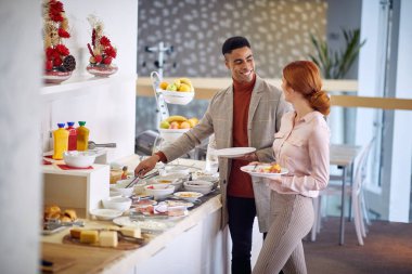 İki genç iş arkadaşı ofiste kahvaltı yapıyor.