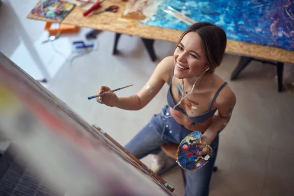 鸟瞰一个年轻性感迷人的女艺术家 心情很好 坐在画架前 在工作室里愉快地欣赏绘画和音乐 工作室 — 图库照片