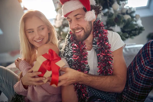 Gülümseyen adam ve kız, Noel ağacının yanında oturup tatilin tadını çıkarıyorlar.