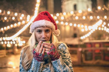 Genç bir kadın Noel 'de panayırda sıcak çay içiyor.