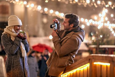 Karlı bir havada, Noel festivalinde gülümseyen bir kız arkadaş çeken bir adam.