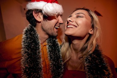 Genç bir çiftin yeni yıl partisinde evdeki şenlikli bir atmosferde kucaklaşırken görüntüsü. Noel, yeni yıl, tatil, parti