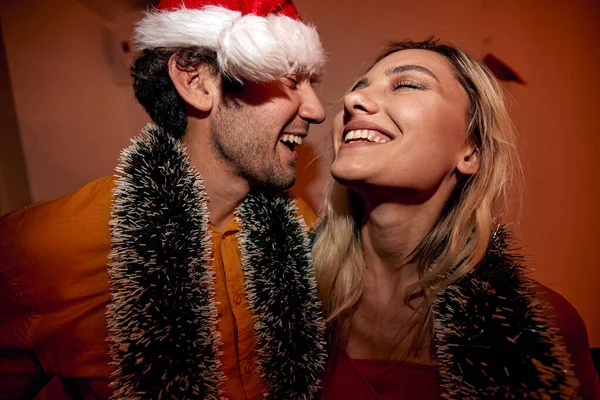 Genç bir çiftin yeni yıl partisinde evdeki şenlikli bir atmosferde kucaklaşırken görüntüsü. Noel, yeni yıl, tatil, parti