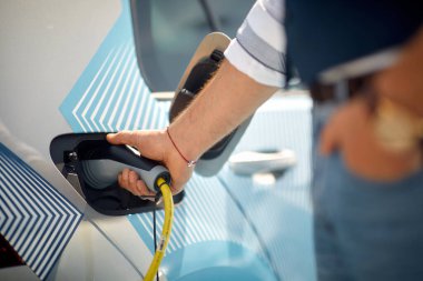 Güzel bir günde istasyonda bir adamın yakın çekimi elektrikli arabasını şarj aletine takmaktır. Araba, elektrik, istasyon.