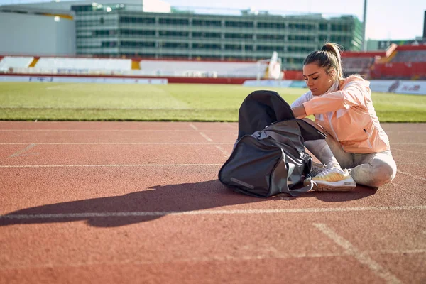 一位年轻女子正坐在跑道上 准备在一个美丽的日子在体育场进行训练 运动员 — 图库照片