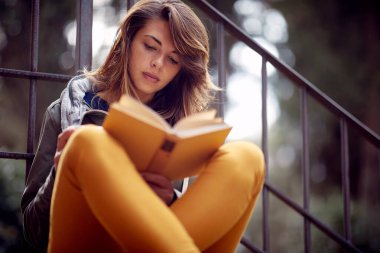 Genç bir kız güzel bir günde binanın önündeki verandada otururken kitap okuyor. Şehir, dışarısı, dinlenme