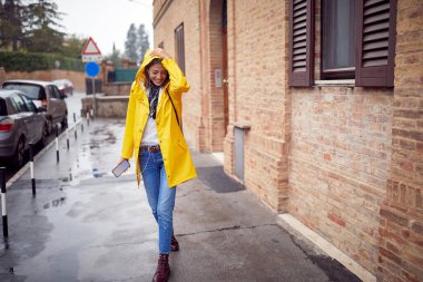 Yağmurda yürüyüp müziğin ve sonbahar gününün tadını çıkarıyorum. Yağmurlu bir günde gülümseyen kadın.