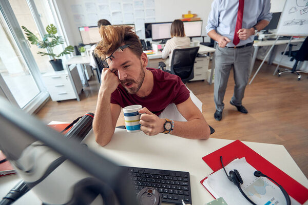 A tired male employee fall asleep while working in a uniform atmosphere in the office. Employees, job, office