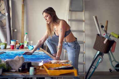 Çok ateşli ve seksi genç bir kadın sanatçı masanın üzerinde duruyor ve stüdyosunda üzerinde çalıştığı bir tabloyu analiz ediyor. Sanat, resim, stüdyo