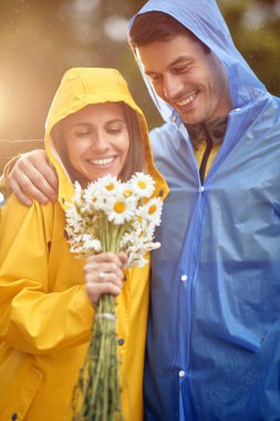 Bir erkeğin çiçek buketini alan bir kadının portresi, yağmurlu bir günde aşk.