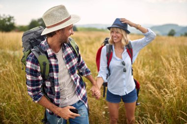 Genç ve neşeli bir çift, güneşli bir günde çayırda yürürken el ele tutuşuyorlar. Yürüyüş, doğa, ilişki, birlikte