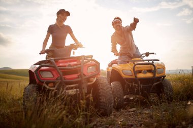 Aşık genç bir çift, doğada güneşli bir günde kuadlara binerken manzaradan zevk alır. Binicilik, ilişki, doğa, aktivite