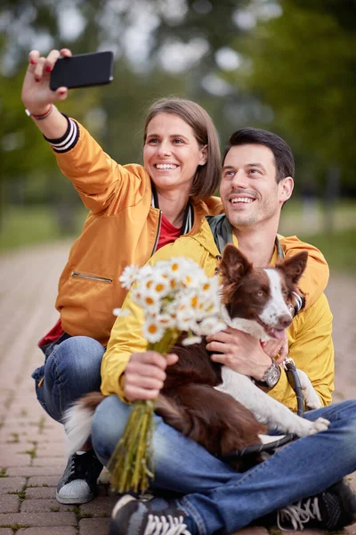 在公园的一条小径上 一对年轻的高加索夫妇抱着自己的狗坐在一条腿上 — 图库照片