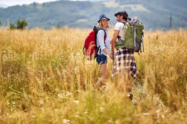 幸せなカップルは山の中でハイキングしています晴れた夏の日に牧草地で楽しい男と女 — ストック写真