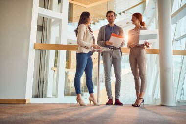Genç bir iş adamı, koridordaki hoş atmosferde iki genç bayan meslektaşıyla eğleniyor. İş, insanlar, şirket.